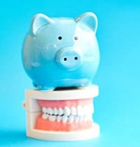 blue piggy bank atop model teeth symbolizing the cost of dental implants in Brampton