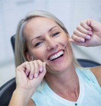 a woman flossing her dental implants at the dentist’s office 