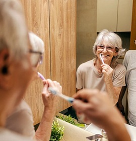 Two denture patients smiling as they brush their teeth 