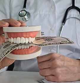 A dentist holding a mock jaw that’s biting a dollar bill