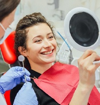 Woman using mirror while visiting implant dentist in Brampton