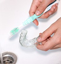 Hands using toothbrush to clean clear aligner