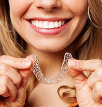 Nose-to-shoulder view of woman smiling holding Invisalign