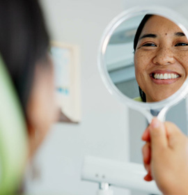 Woman smiling at reflection in handheld mirror