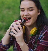 Young woman using her teeth to open bottle