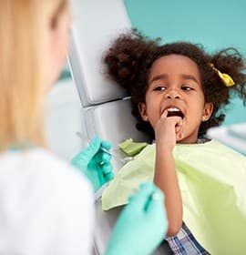 Child in dental chair pointing to teeth