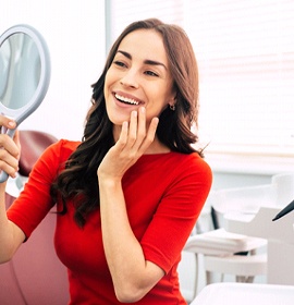 Woman smiling in mirror after smile makeover in Brampton