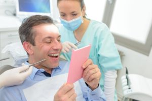 man in dental chair looking at teeth in mirror